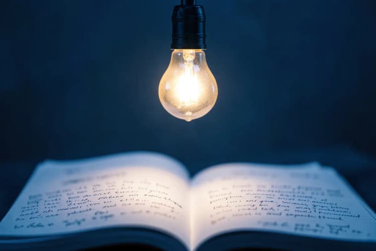 Lâmpada acesa sobre um bloco de notas com ideias.