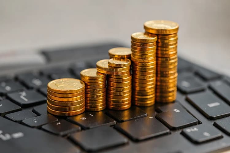 Um gráfico de barras ascendente feito de moedas de ouro empilhadas, em cima de um teclado de computador.