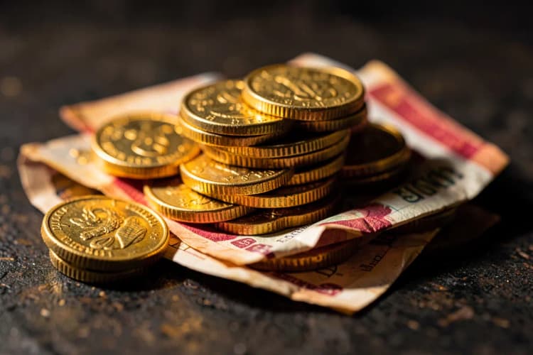 Uma pilha de moedas de ouro e notas de dinheiro dobradas em uma superfície escura.