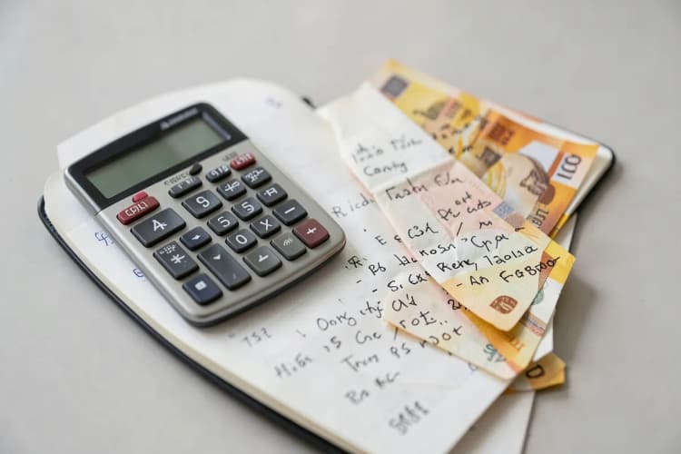 Uma calculadora e notas de dinheiro sobre um caderno aberto com anotações, simulando custos de anúncios.