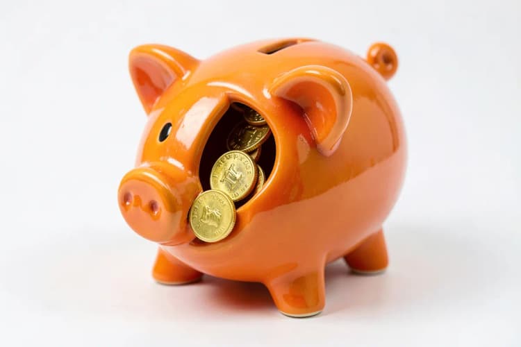 Um cofrinho em forma de porco com moedas de ouro caindo dentro dele, em um fundo branco.