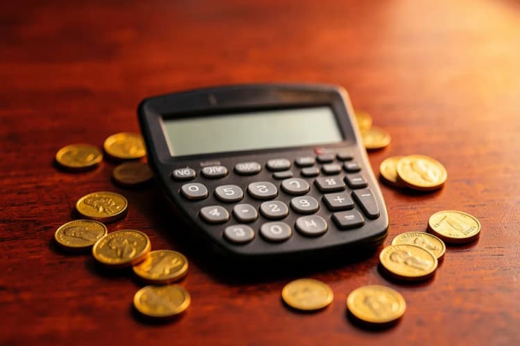 Calculadora e moedas de ouro espalhadas em uma superfície de madeira escura, close-up, luz de estúdio vindo da direita, sem ação.